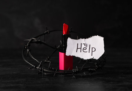 Paper piece with word HELP, lipstick and barbed wire on dark background. Domestic violence conceptの写真素材