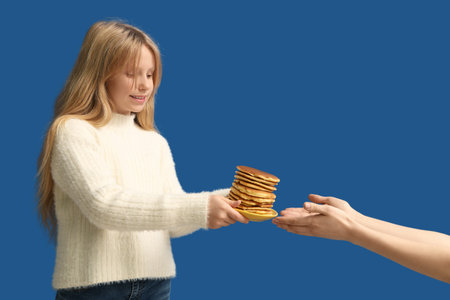 Little girl giving tasty pancakes away on blue background