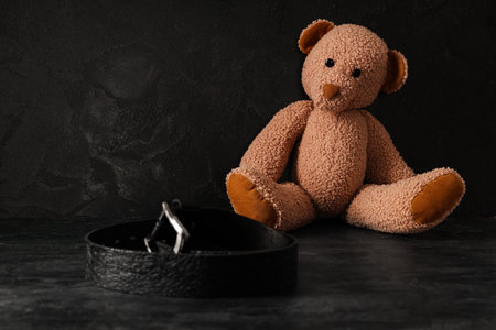 Toy bear with belt on dark background. Domestic violence conceptの写真素材
