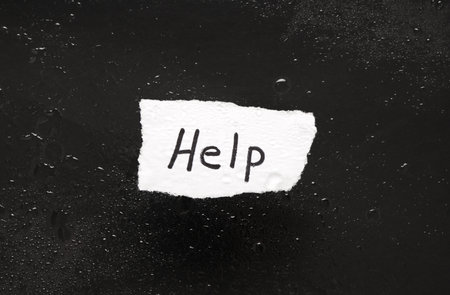 Paper piece with word HELP in water on dark background. Domestic violence conceptの写真素材