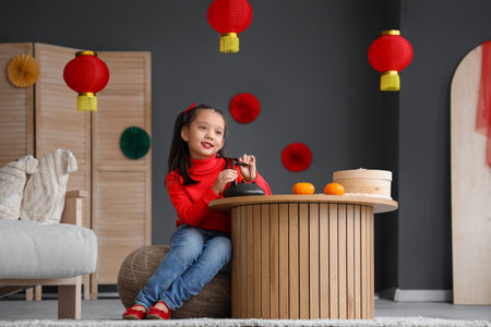 Cute little Asian girl with teapot celebrating Chinese New Year at homeの写真素材