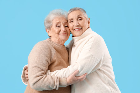 Senior female friends hugging on blue backgroundの写真素材