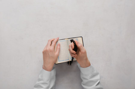 Female hands with Koran and prayer beads for Ramadan on white grunge backgroundの写真素材