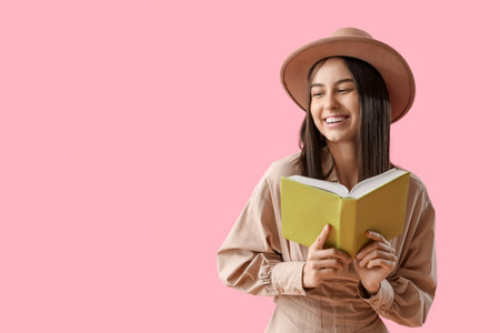 Young woman in hat with book on pink backgroundの写真素材