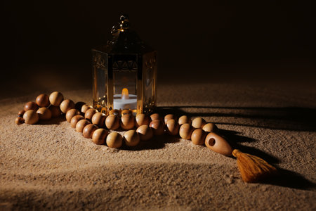 Muslim lamp with burning candle and prayer beads for Ramadan on sand against dark backgroundの写真素材
