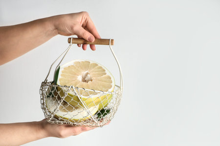 Female hands with basket of fresh pomelo fruits on white background