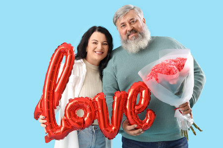 Beautiful mature couple with roses bouquet and balloon in the shape of the word LOVE on blue...