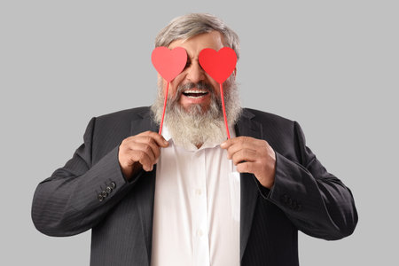 Beautiful happy mature man with paper hearts on gray background. Valentine's Day celebrationの写真素材