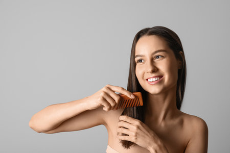 Pretty woman combing hair on gray backgroundの写真素材