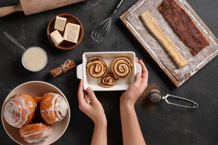 Female hands with ingredients and kitchen utensils for cooking cinnamon buns on black grunge backgroundの写真素材