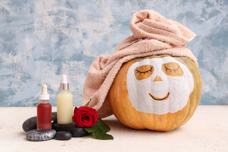 Pumpkin with drawn face, serum, towel, rose and clay mask on white tableの写真素材