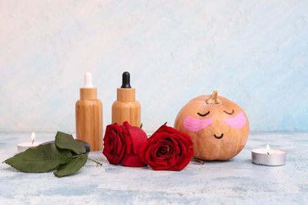 Pumpkin with drawn face, under-eye patches, spa supplies and roses on grunge blue tableの写真素材
