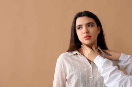Endocrinologist examining thyroid gland of young woman on beige background