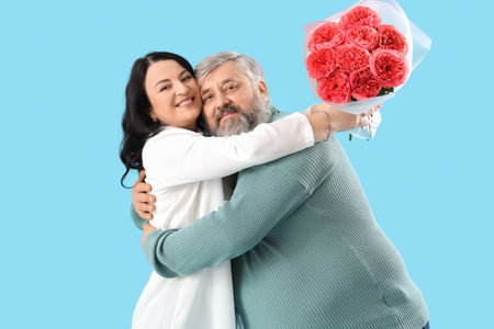 Beautiful mature couple with bouquet of roses hugging on blue background. Valentine's Day celebrationの写真素材