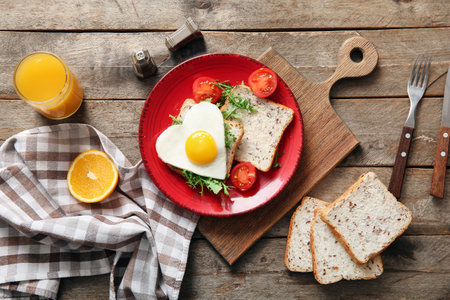 Plate with tasty fried egg, toasts, tomatoes and glass of juice on wooden backgroundの写真素材