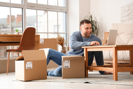 Young man with parcels using laptop at homeの写真素材