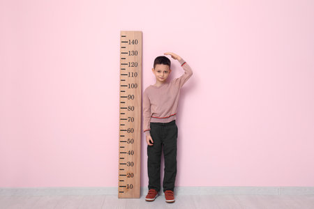 Cute little boy measuring height near pink wallの写真素材