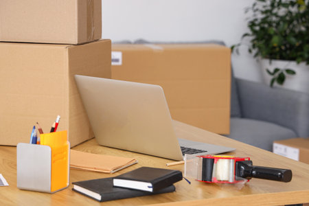 Laptop with adhesive tape and parcels on table in warehouse storeの写真素材