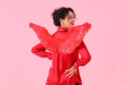 Young African-American woman with Cupid's wings on pink background, back view. Valentine's Day celebrationの写真素材