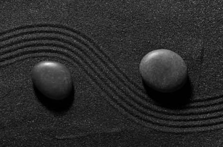 Stones on dark sand with lines in Japanese rock garden, top view. Zen concept