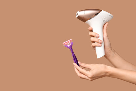 Female hands with modern photoepilator and razor on brown backgroundの写真素材