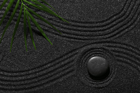 Stone and tropical leaf on dark sand with lines in Japanese rock garden, top view. Zen concept