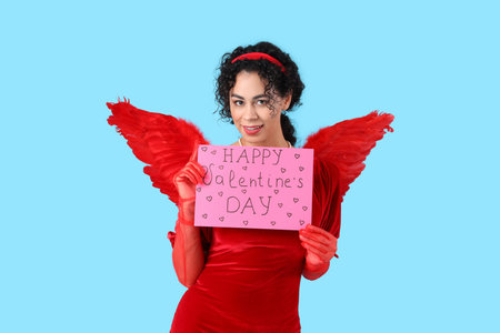Young African-American woman dressed as Cupid with card for Valentine's Day on blue background