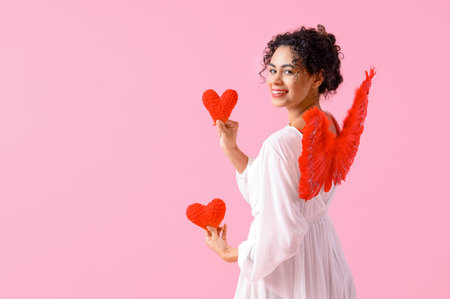Young African-American woman dressed as Cupid with hearts on pink background. Valentine's Day...