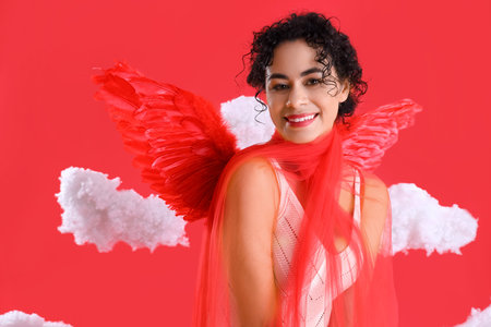 Young African-American woman dressed as Cupid in clouds on red background. Valentine's Day...