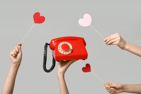 Female hands holding vintage telephone and paper hearts on gray background. Valentine's Day celebrationの写真素材