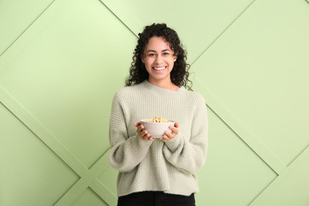 Happy young woman with bowl of cereal rings against color wallの写真素材