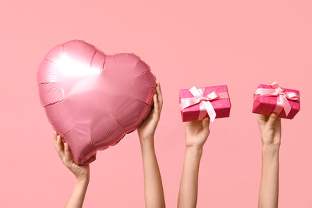 Female hands holding heart-shaped balloon and gift boxes on pink background. Valentine's Day celebrationの写真素材