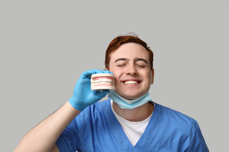 Male dentist with jaw model on gray background. World Dentist Day