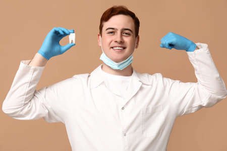 Male dentist with tooth model flexing on beige background. World Dentist Dayの写真素材