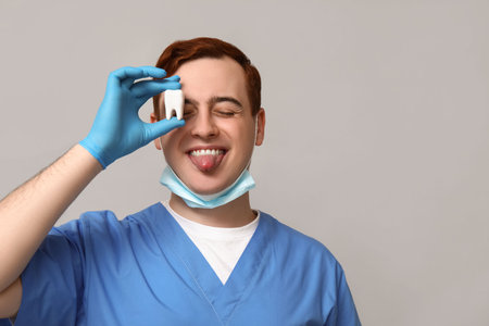 Male dentist with tooth model on gray background. World Dentist Day
