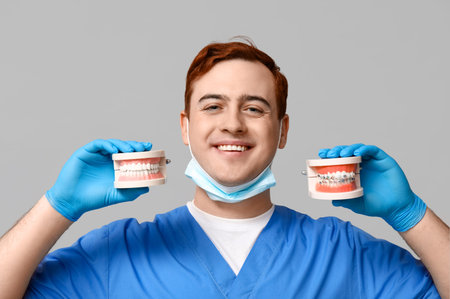 Male dentist with jaw models on gray background. World Dentist Day