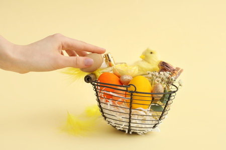 Female hand with basket full of bottles of perfumes, Easter eggs and baby chicken on yellow...