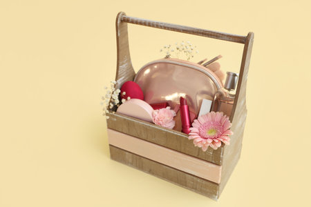 Wooden basket with decorative cosmetics, Easter eggs and flowers on yellow backgroundの写真素材