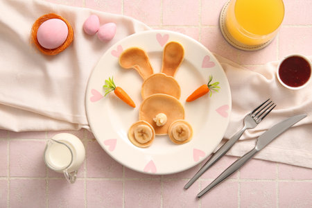 Funny Easter bunny pancakes with glass of orange juice and painted eggs on pink tile backgroundの写真素材