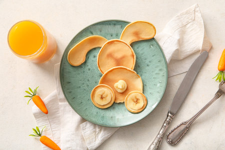 Funny Easter bunny pancakes with glass of orange juice on white tile backgroundの写真素材