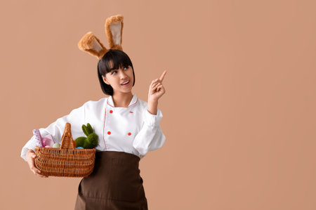 Female chef in bunny ears with Easter eggs pointing at something on brown backgroundの写真素材