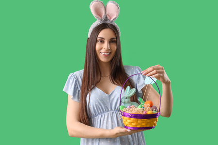 Young pregnant woman in bunny ears with Easter eggs on green backgroundの写真素材