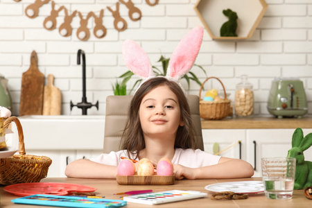 Cute little girl with bunny ears painting Easter eggs at home