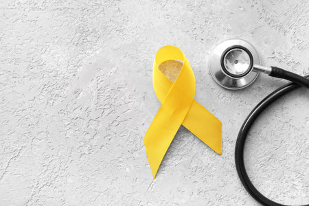 Golden ribbon with stethoscope on light grunge background. Children cancer awareness conceptの写真素材