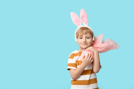 Cute little boy in bunny ears with Easter gift egg on blue background