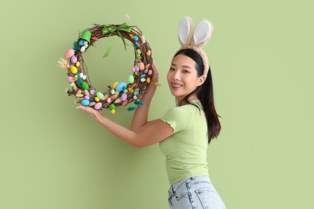 Young Asian woman in bunny ears with Easter wreath on green backgroundの写真素材