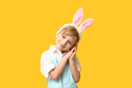 Cute little boy in bunny ears on yellow backgroundの写真素材