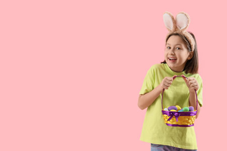 Little girl in bunny ears with basket of Easter eggs on pink background