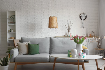 Vases with tulips, Easter rabbit and eggs on table in living room