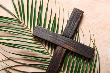 Wooden cross with palm leaf on beige background